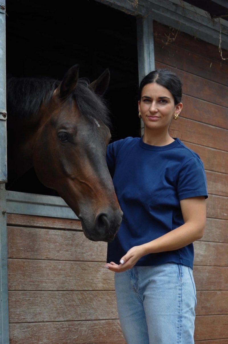 Jeanne François aux côtés d'un cheval bai devant une écurie
